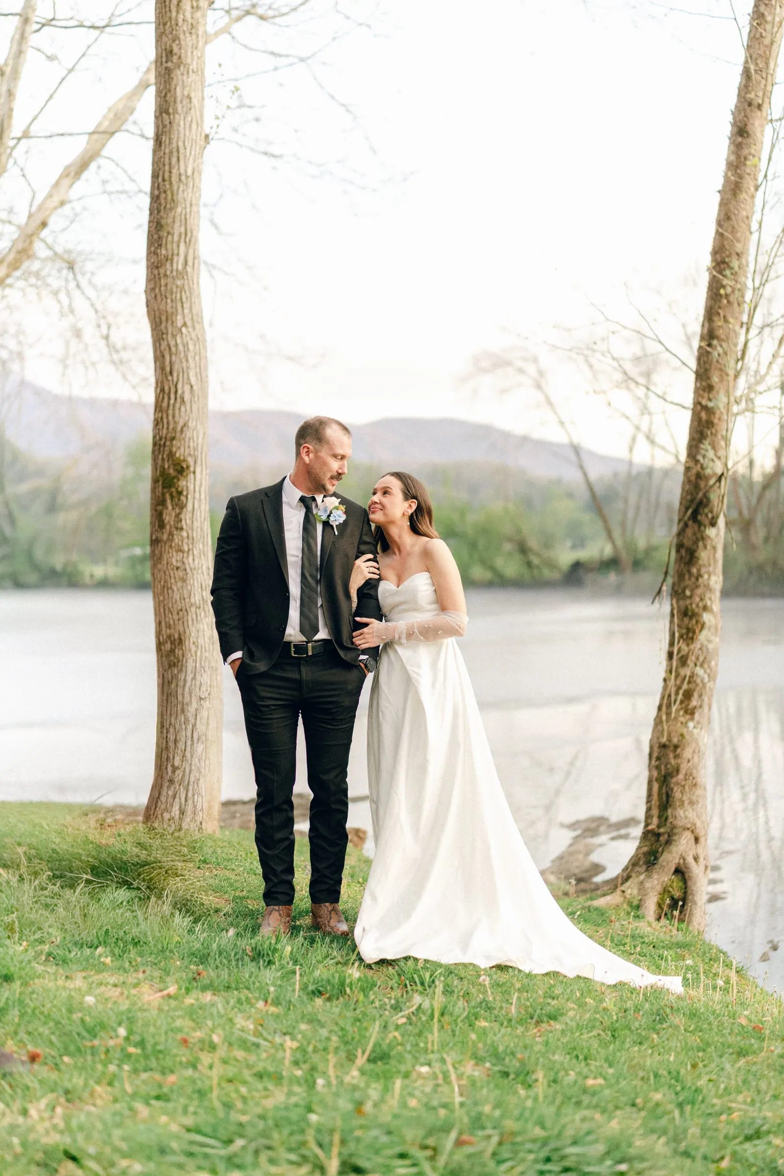 A couple standing together by the South Holston River with the mountains behind them