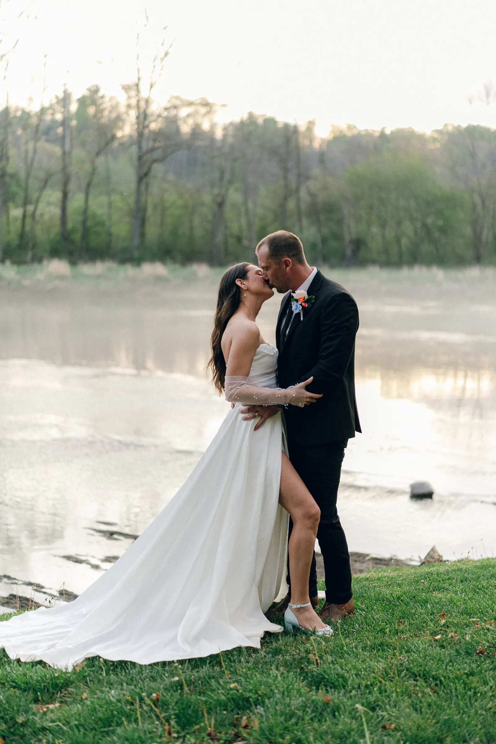Couple kissing on the misty riverbank at golden hour