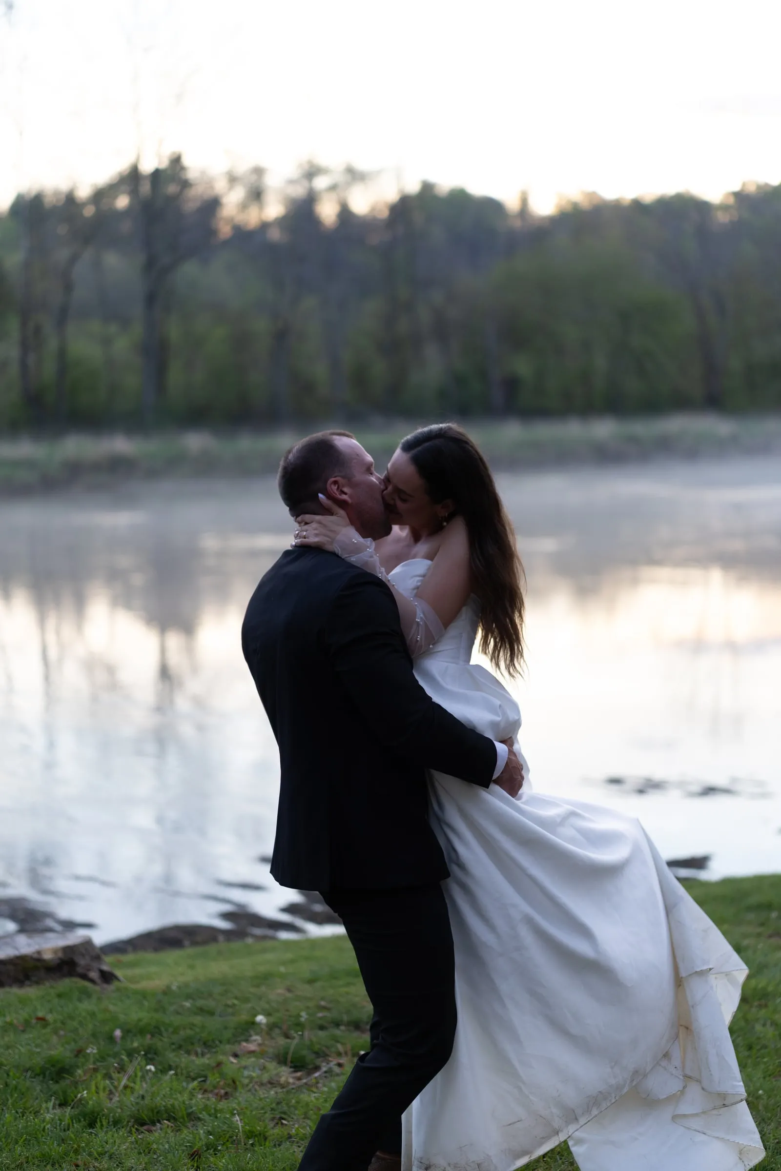 Groom dipping the bride for a kiss beside the misty river