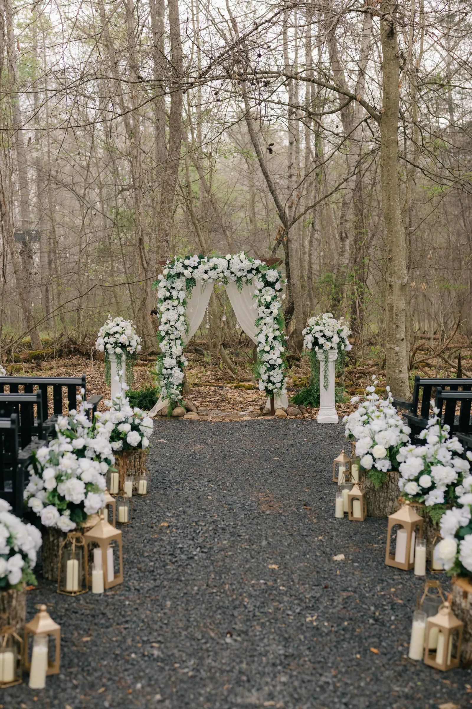 Lantern-lined ceremony aisle leading to a floral arch in misty woodland