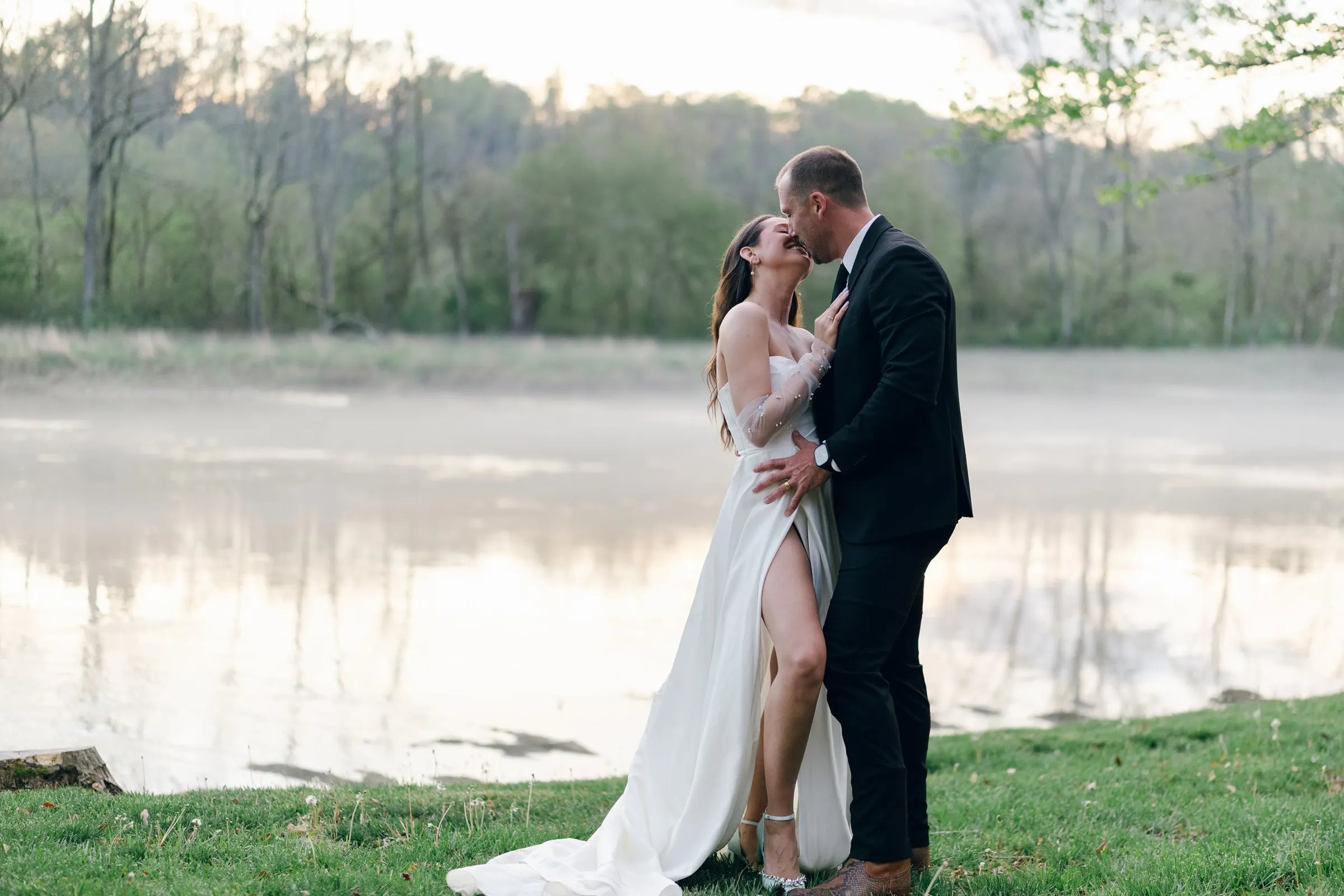 Wide photo of the couple kissing on the misty river at golden hour