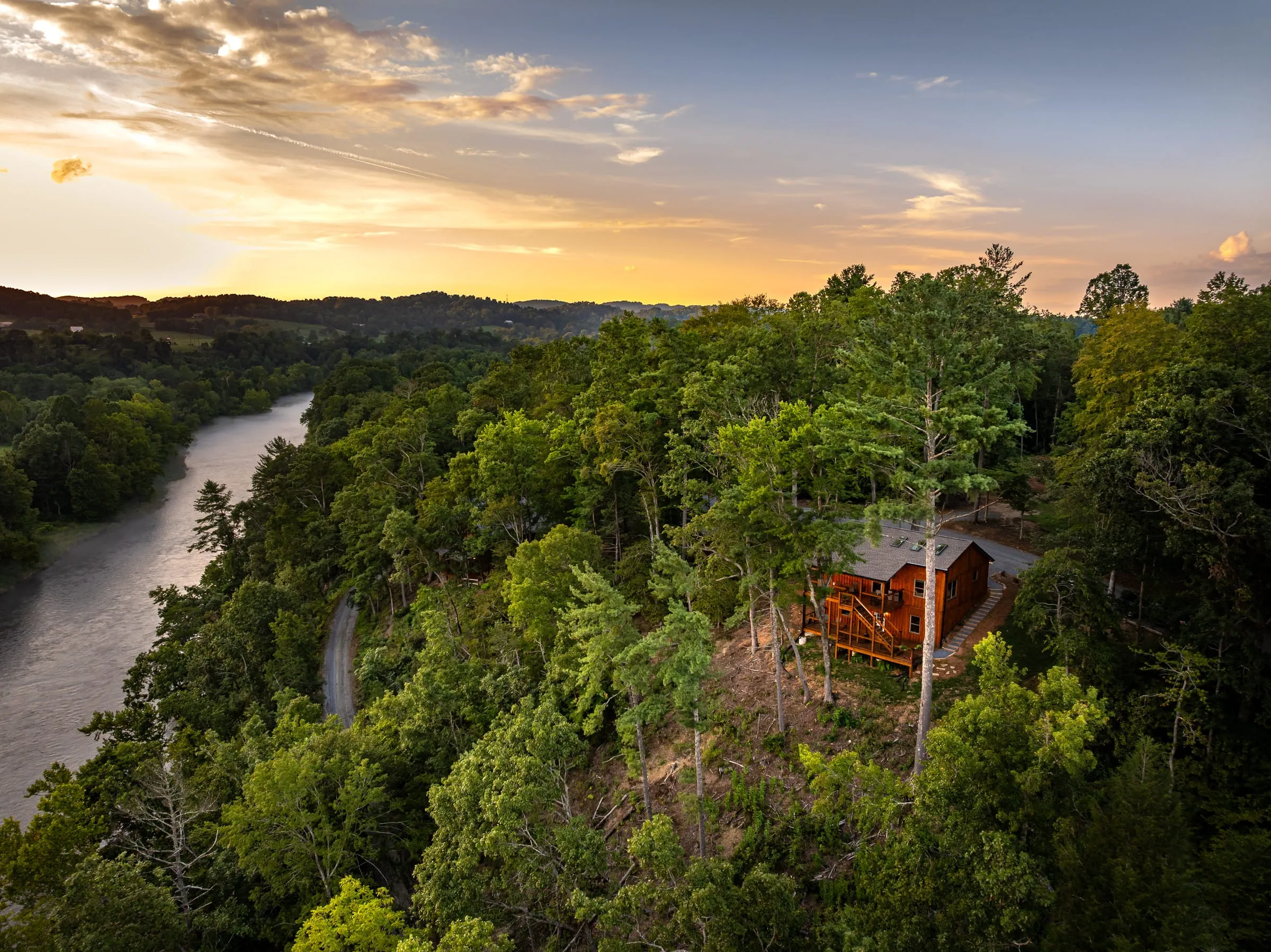 Aerial view of a riverside cabin tucked into the trees at sunset